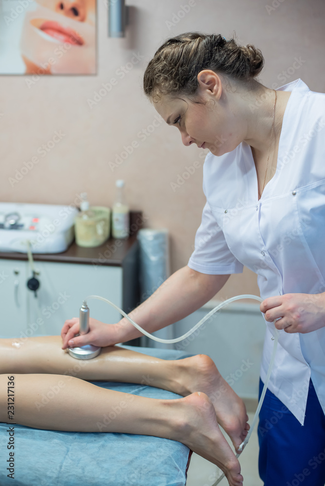 Obraz premium The doctor-cosmetologist performs a vacuum-roll massage of the buttocks and legs of a young woman. Masseuse does her job with the help of the apparatus of correction