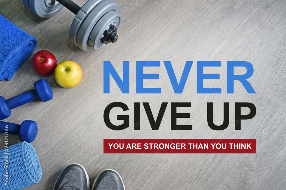 Never Give Up. You Are Stronger Than You Think. Fitness motivational quotes.Sport  theme. Healthy and active lifestyle concept. Sneakers, dumbbells, apples  and a workout mat on grey wooden background. Stock Photo