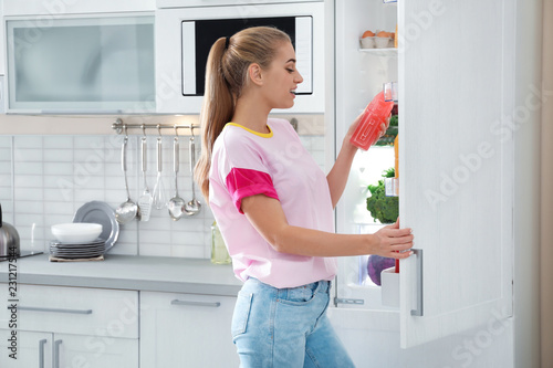Woman taking bottle of juice out of refrigerator in kitchen