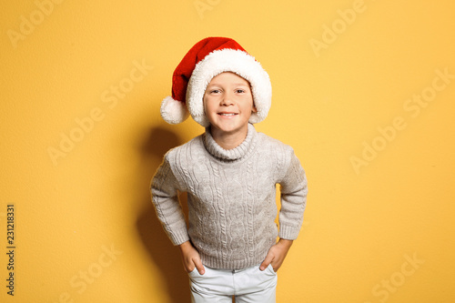 Cute little boy in warm sweater and Christmas hat on color background © New Africa