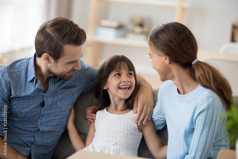 Attractive multi-ethnic young family with child sitting on sofa in living room at new home. Parents talking communicating with adorable small daughter feels happy excited enjoying free time together Attractive multi-ethnic young family with child sitting on sofa in living room at new home. Parents talking communicating with adorable small daughter feels happy excited enjoying free time together