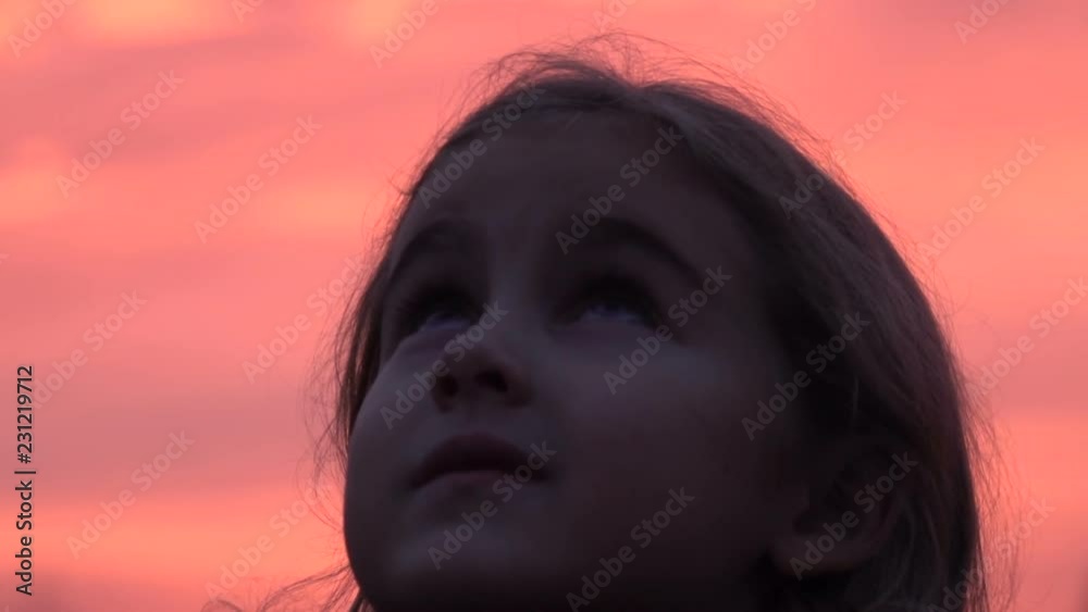 Kid looking up at the sky in nature. Little girl praying looking up at purple sky with hope, close-up. Kid looking up at the sky in nature. Little girl praying looking up at purple sky with hope, close-up.