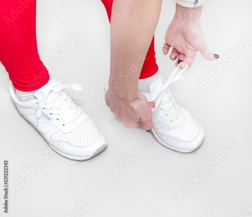 Girl tying white sneakers on a light background