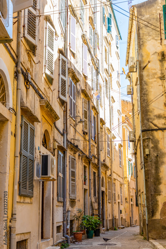 View of typical narrow street of an old town of Corfu, Greece. Close-up of facade of old tenement houses with window shutters.