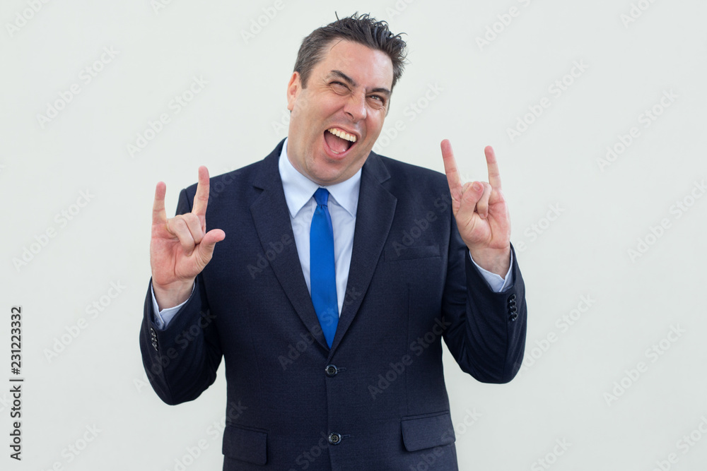 Jolly cool businessman showing signs of horns and having fun. Cheerful middle-aged man in suit gesturing hands and screaming in excitement. Cool man concept Jolly cool businessman showing signs of horns and having fun. Cheerful middle-aged man in suit gesturing hands and screaming in excitement. Cool man concept