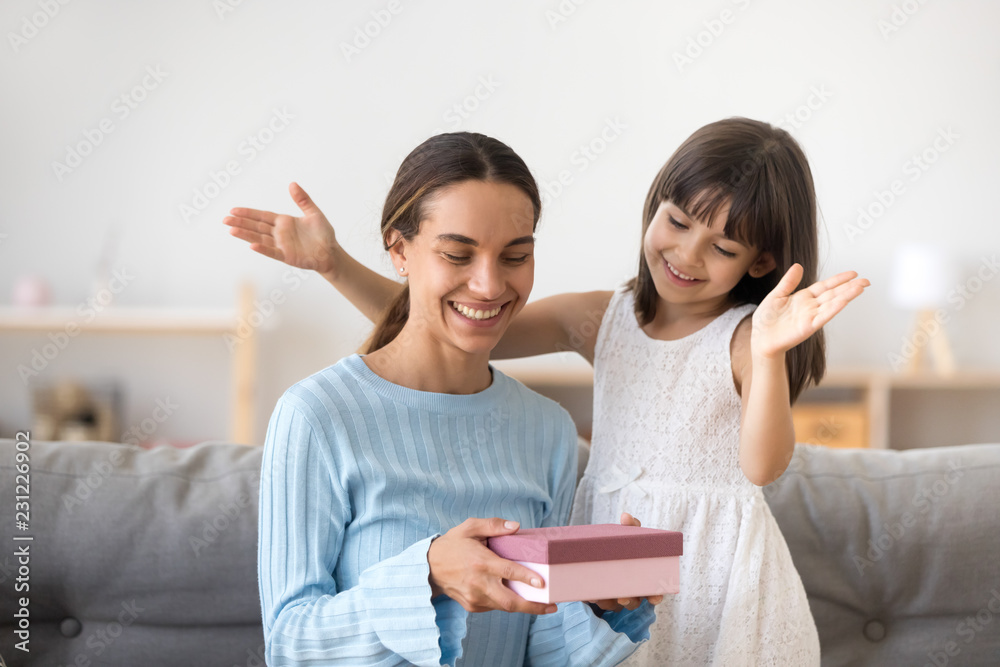 Young mother receives from adorable smiling daughter a gift, female feels happy and excited holding pink gift box. Kid make a surprise for loving mom. Life events mother day and celebrations concept Young mother receives from adorable smiling daughter a gift, female feels happy and excited holding pink gift box. Kid make a surprise for loving mom. Life events mother day and celebrations concept