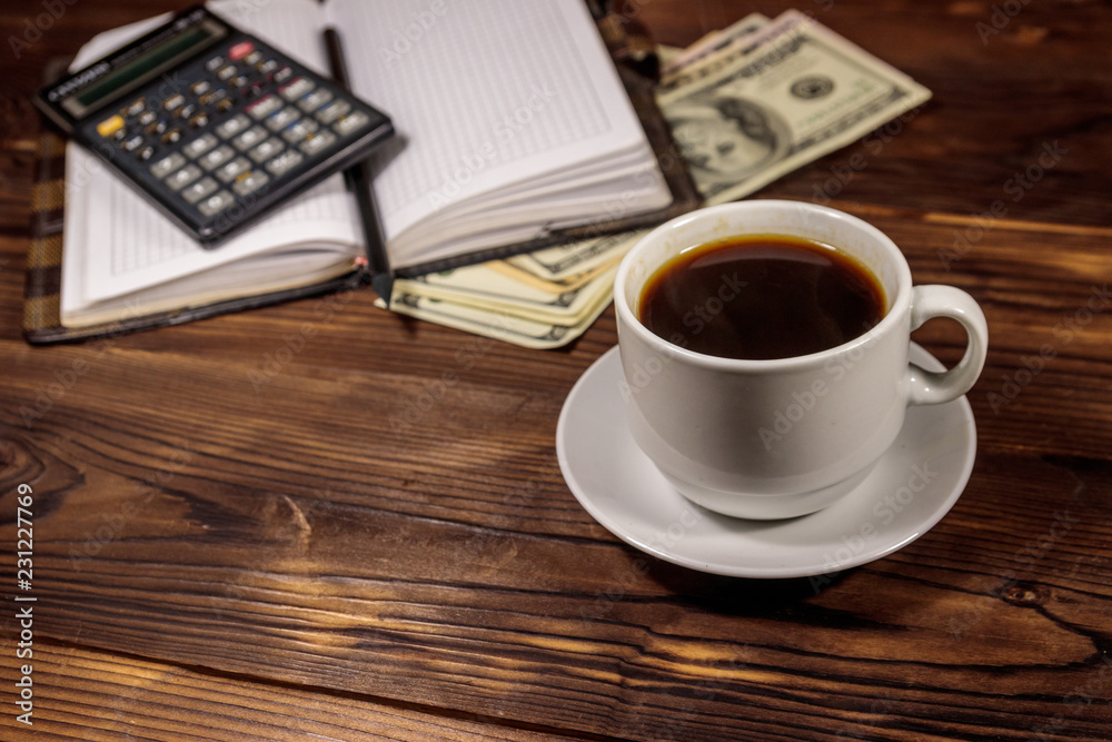 Cup of coffee and notepad with dollars, pencil and calculator on wooden desk. Financial concept Cup of coffee and notepad with dollars, pencil and calculator on wooden desk. Financial concept