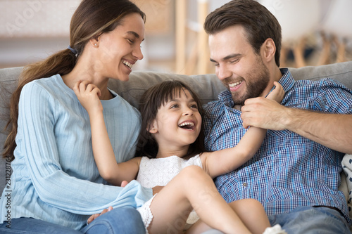Close up smiling cheerful daughter tickling parents people have fun playtime together at home. Parents laughing enjoy weekend with little adorable kid. Happy parenting love friendly relations concept