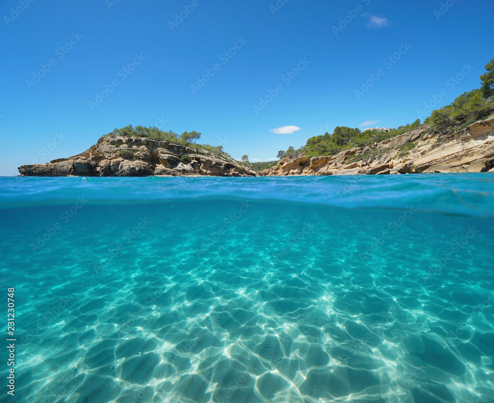 Obraz premium Rocky coast with an islet and sand underwater, split view half above and below water surface, Mediterranean sea, Catalonia, l'Illot, L'Ametlla de Mar, Tarragona, Costa Dorada, Spain