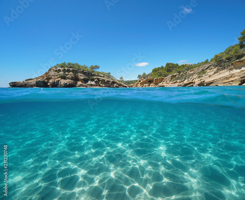 Rocky coast with an islet and sand underwater, split view half above and below water surface, Mediterranean sea, Catalonia, l'Illot, L'Ametlla de Mar, Tarragona, Costa Dorada, Spain