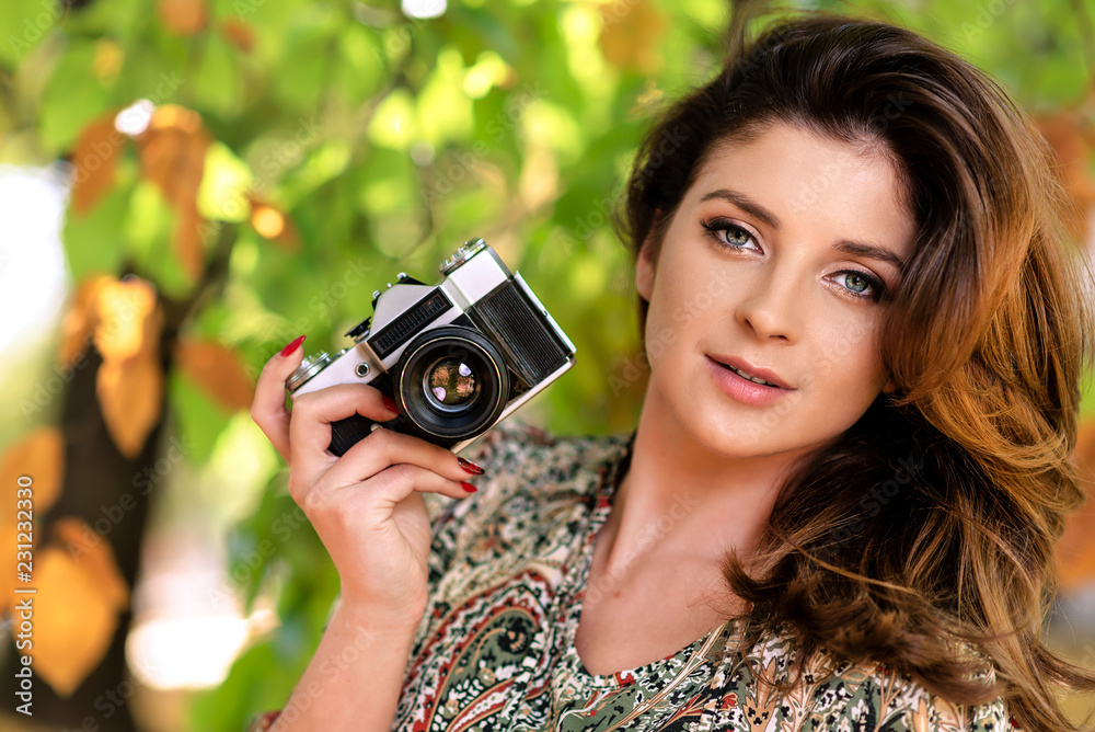 Beautiful and lovely woman holding a retro SLR camera and taking photos in an autumn park on a sunny day Beautiful and lovely woman holding a retro SLR camera and taking photos in an autumn park on a sunny day