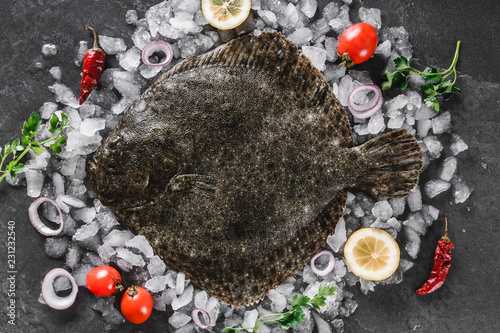 Tableau sur toile Raw whole flounder fish with spices on ice over dark stone background