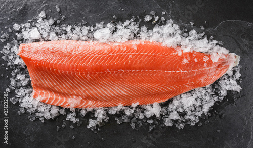 Fresh raw salmon fish steak with spices on ice over dark stone background. Creative layout made of fish, top view, flat lay photo