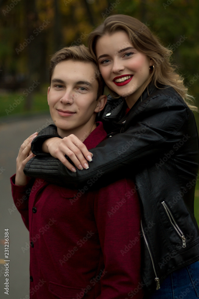 girl in a black jacket, smiling, hugging a guy. couple in love in the autumn park. family on vacation, date, lovers. hug from the back, come from the back. girl in a black jacket, smiling, hugging a guy. couple in love in the autumn park. family on vacation, date, lovers. hug from the back, come from the back.