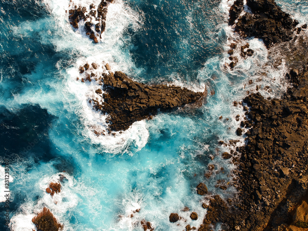 Obraz premium Aerial top view of sea waves hitting black volcanic rocks on the coastline with turquoise sea water. Amazing rock cliff seascape in the Portuguese coastline. Azores islands. Drone shot.