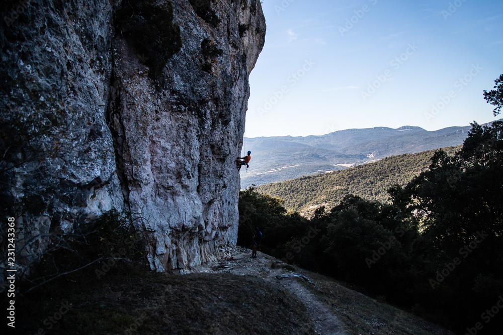 Young climber man climbing a large wall in a beautiful landscape in shadow 