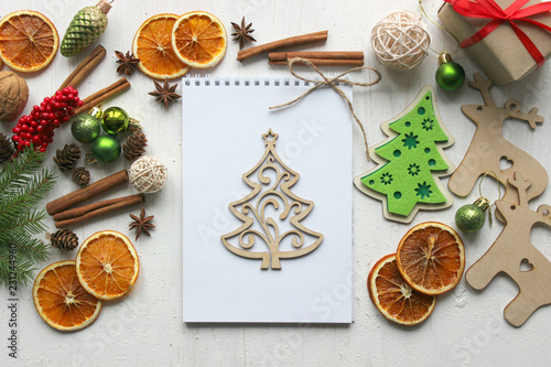 Christmas card, white paper notebook background surrounded by Christmas balls, fir branches, cinnamon sticks, spices, dried orange, wooden deer . Copy space.