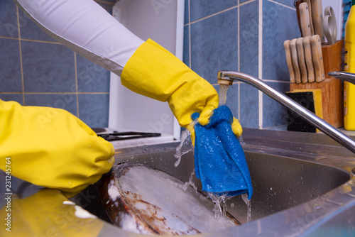 a woman with a rubber yellow glove washes a blue cloth in the sink