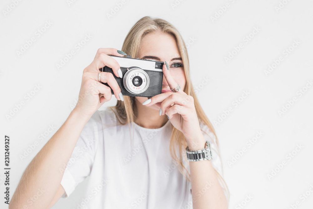 Portrait of a young stylish blonde girl using and taking pictures on an old vintage camera on a white background Portrait of a young stylish blonde girl using and taking pictures on an old vintage camera on a white background