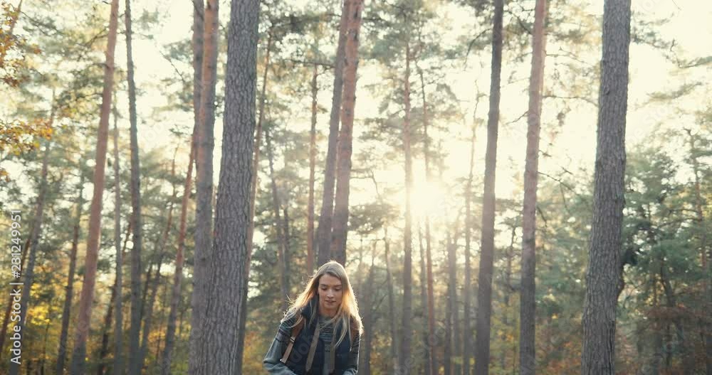 Young pretty blonde woman with camera coming in the middle of the forest on the small hill and her boyfriend following her in autumn. Outdoors. Young pretty blonde woman with camera coming in the middle of the forest on the small hill and her boyfriend following her in autumn. Outdoors.