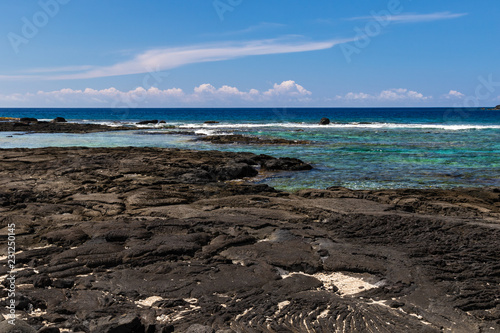 View of Blue Pacific ocean from Puuhonua o Honaunau Historical Park, Big Island, Hawaii. Crystal blue-green water in the bay; coastline in the background, volcanic rock and sand in foreground. photo