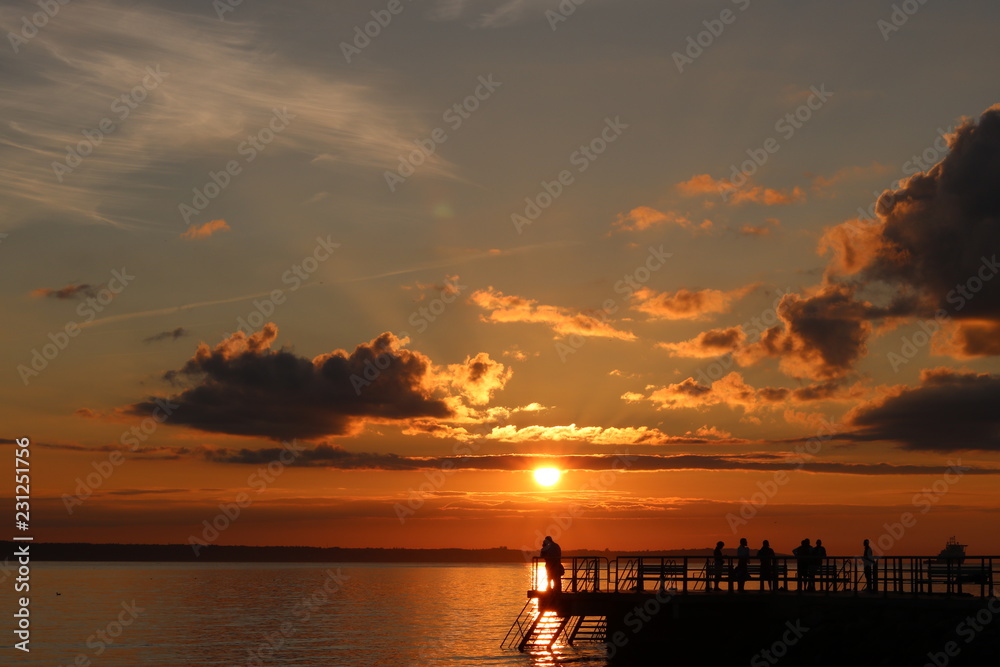 people on pier admiring sunset towards horizon