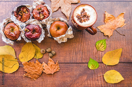 backed apples in foil with cup of coffee and autumn leaves on wooden background