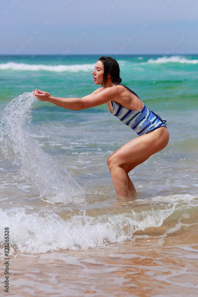 Fototapeta premium Beautiful young woman in swimsuit scooping ocean joy