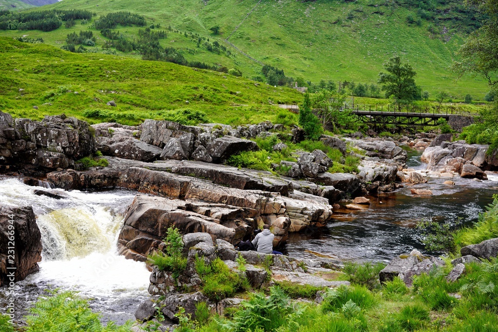 Durch schottisches Tal fließt ein wilder Bach darin Felsen und Steine