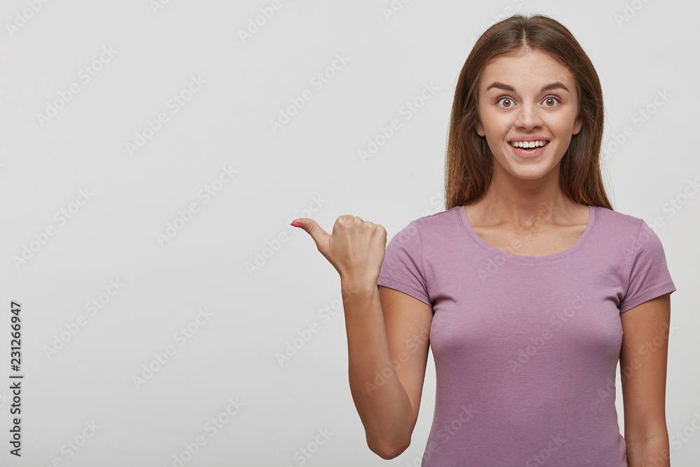 Surprised funny teenage girl showing empty copy space with her thumb finger,place for advertisement or text, isolated over white background. Happy girl pointing, looking at camera Surprised funny teenage girl showing empty copy space with her thumb finger,place for advertisement or text, isolated over white background. Happy girl pointing, looking at camera