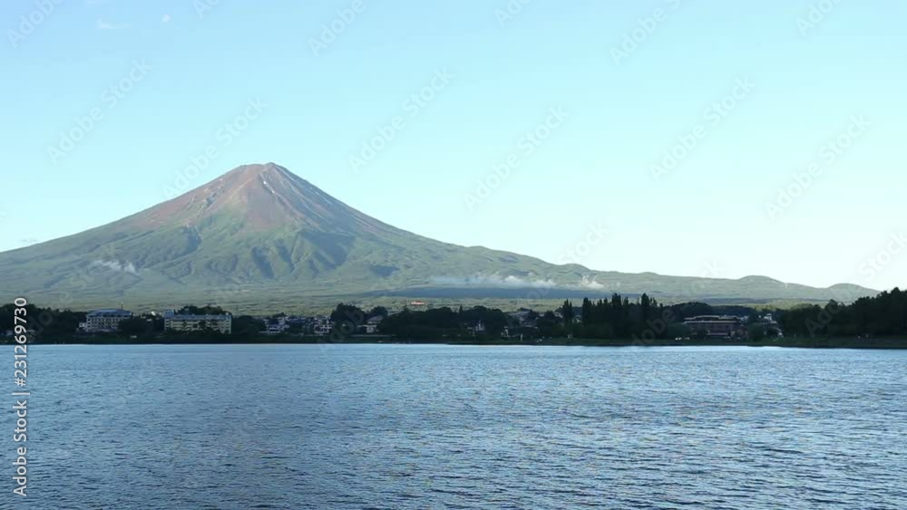 Summertime Mt. Fuji brown peak off-center on clear blue sky morning with small moving clouds above serene water of Kawaguchiko and distant shoreline hotel buildings in Japan. Stationary 30fps 1080 HD Summertime Mt. Fuji brown peak off-center on clear blue sky morning with small moving clouds above serene water of Kawaguchiko and distant shoreline hotel buildings in Japan. Stationary 30fps 1080 HD