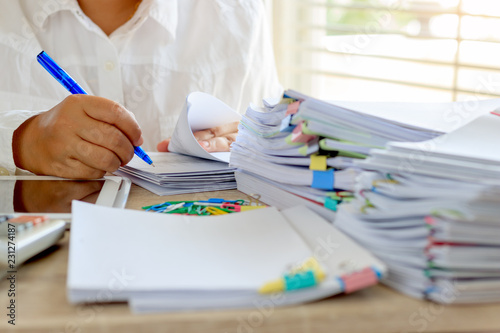 Teacher is checking student homework assignment and report on desk in school for score. Unfinished paperwork stacked in archive with color papers and paper clips. Education and business concept.