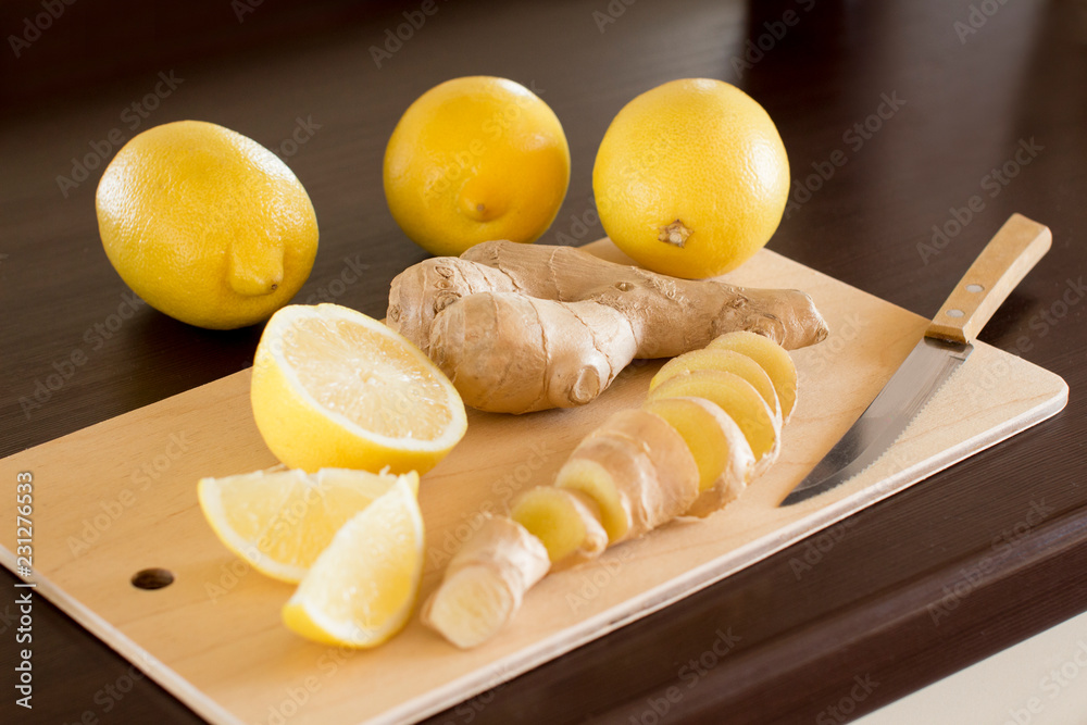 sliced lemons and ginger root on a wooden cutting board on a dark wooden kitchen table sliced lemons and ginger root on a wooden cutting board on a dark wooden kitchen table
