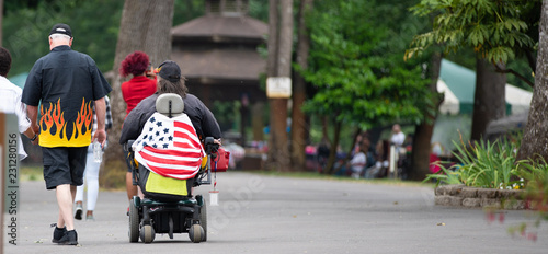 Elderly woman in a wheelchair draped in american flag during fourth of july celebration.