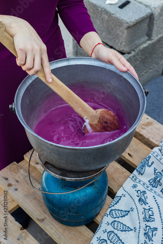 Cooking grape juice, corn and white flour in big pot boiler mixing with wooden spoon for pelamushi, tatara or churchkhela - traditional Georgian dessert sweets with walnuts or hazelnuts. photo