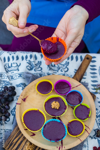 Pelamushi - Gerogian traditional sweet dessert. Cooked porridge with condensed grape juice, corn and white flour, walnuts. Woman hands take with spoon and hold tatara in silicone pie tin.  photo