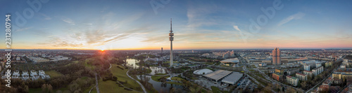 Weites Panorama von München mit dem Olympiapark aus der Luft samt Olympiaturm, BMW Welt und Museum, Olympiasee zum Sonnenuntergang am Abend