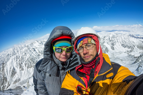 Selfie couple climber in helmet and down jacket stand on top of mountain