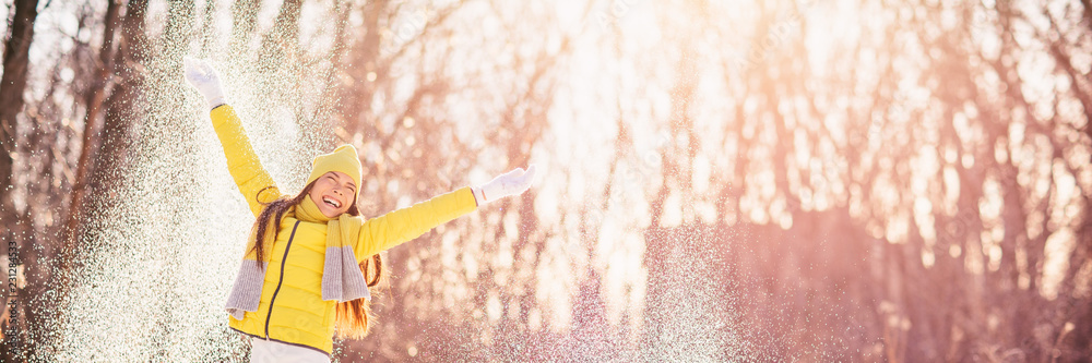 Naklejka premium Happy winter girl playing outside throwing snow outdoor in forest having fun - banner panorama lifestyle.