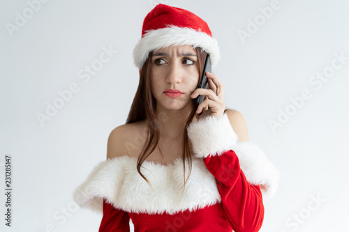 Concerned Christmas girl speaking on phone. Beautiful young woman in Santa hat speaking on mobile phone. Communication concept