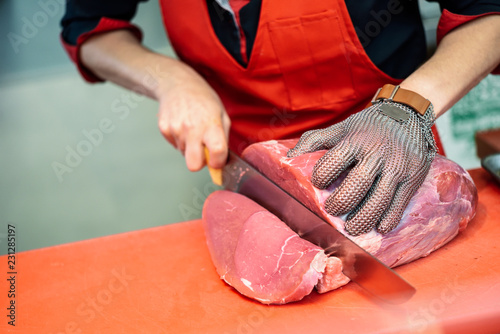 Принти на полотні Woman cutting fresh meat in a butcher shop with metal safety mesh glove
