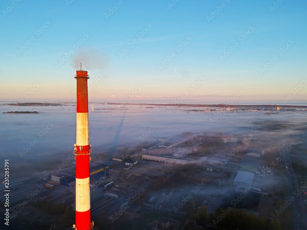 Fototapeta premium Aerial view on brick chimney and city covered in fog.