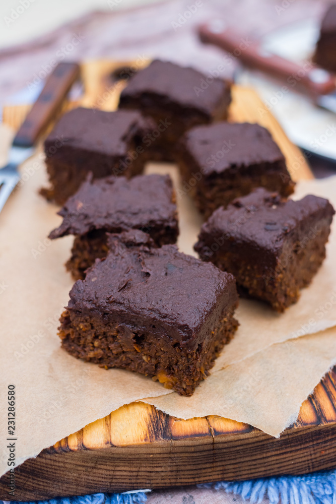 Vegan chocolate sweet brownie cake on wooden kitchen board and parchment paper. Pumpkin, cacao powder, Iranian dates. No bake. Vegetarian raw dessert piece. Paleo diet. Healthy food Vegan chocolate sweet brownie cake on wooden kitchen board and parchment paper. Pumpkin, cacao powder, Iranian dates. No bake. Vegetarian raw dessert piece. Paleo diet. Healthy food