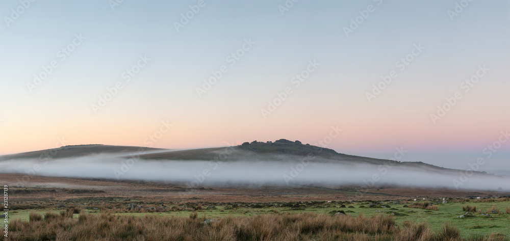 Beautiful foggy sunrise landscape over the tors in Dartmoor revealing peaks through the mist