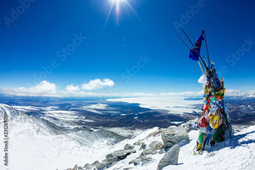 Tibetstkimi post with the flags on the top of a mountain with views of the icy lake © Baikal360