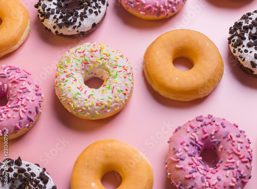 Top view of many colorful donuts on pink background.