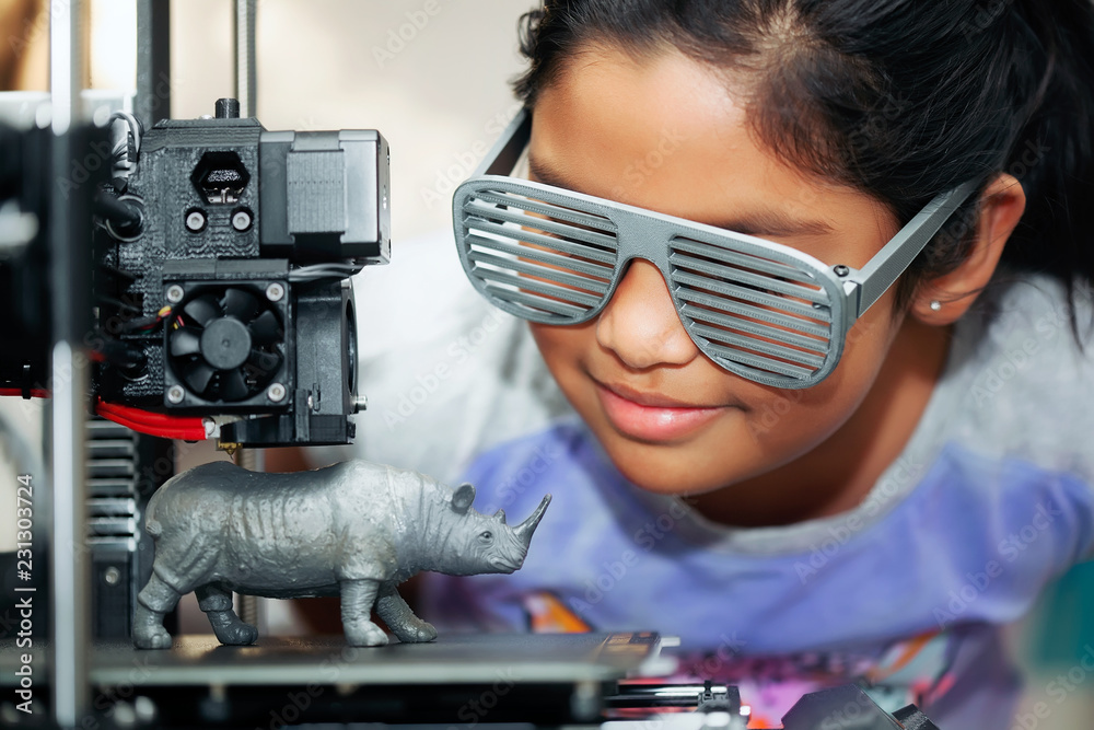 Cute girl with cool 3d printed shutter shades is watching her 3d printer as it prints her 3d model of a rhinoceros. - obrazy, fototapety, plakaty 