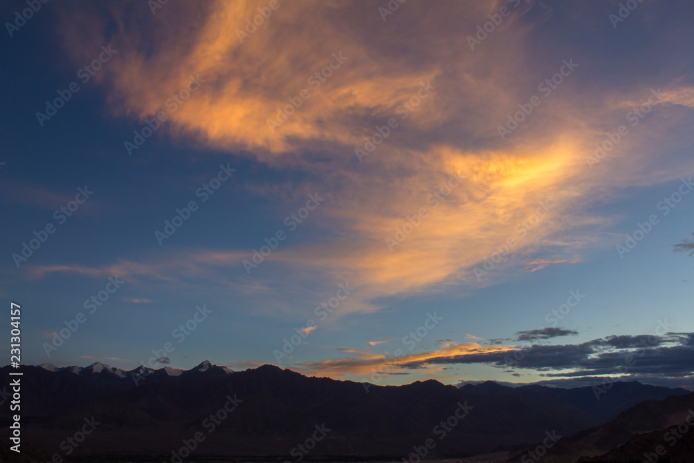 bright orange clouds in the evening sky over a mountain range with snowy peaks