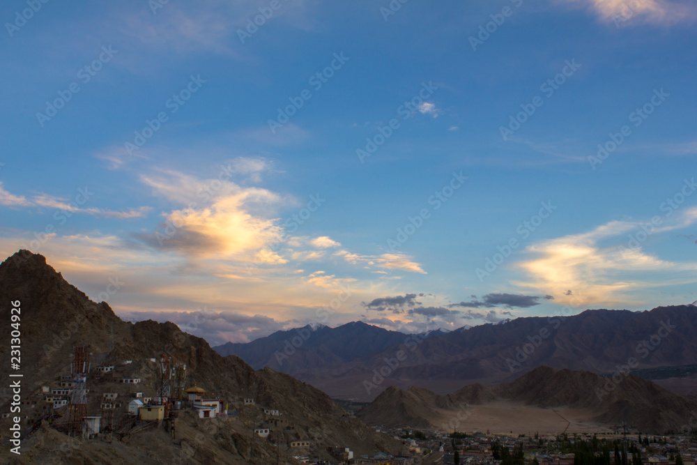 bright colored clouds in the dark blue sky during sunset over the mountains and houses