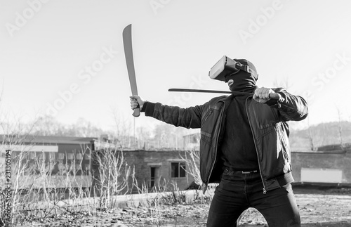 The guy in the mask, leather jacket and virtual reality glasses waving swords machete on the roof of an abandoned city building